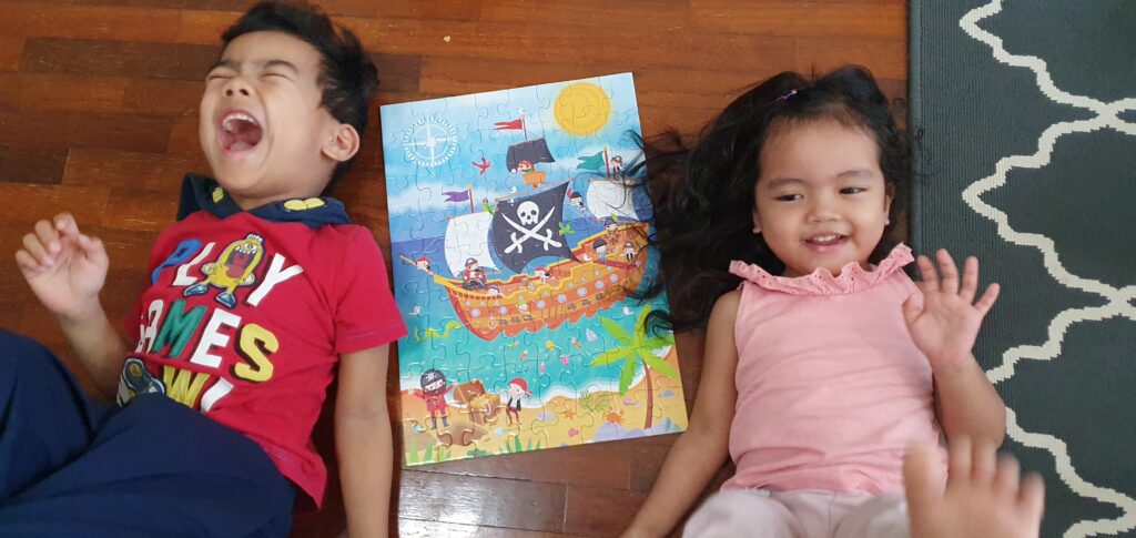 Two children lying on the floor, overjoyed about a pirate puzzle they have completed.