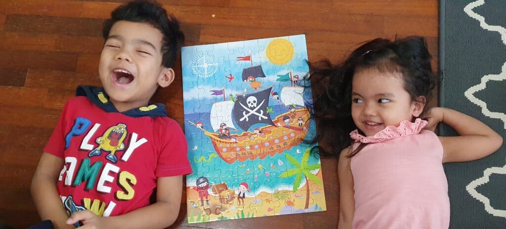 Two kids are lying on the floor, excited about a pirate puzzle. Without a photographer checklist, beginner photographers will spend a lot of time, like these kids, trying to solve the photography jigsaw puzzle